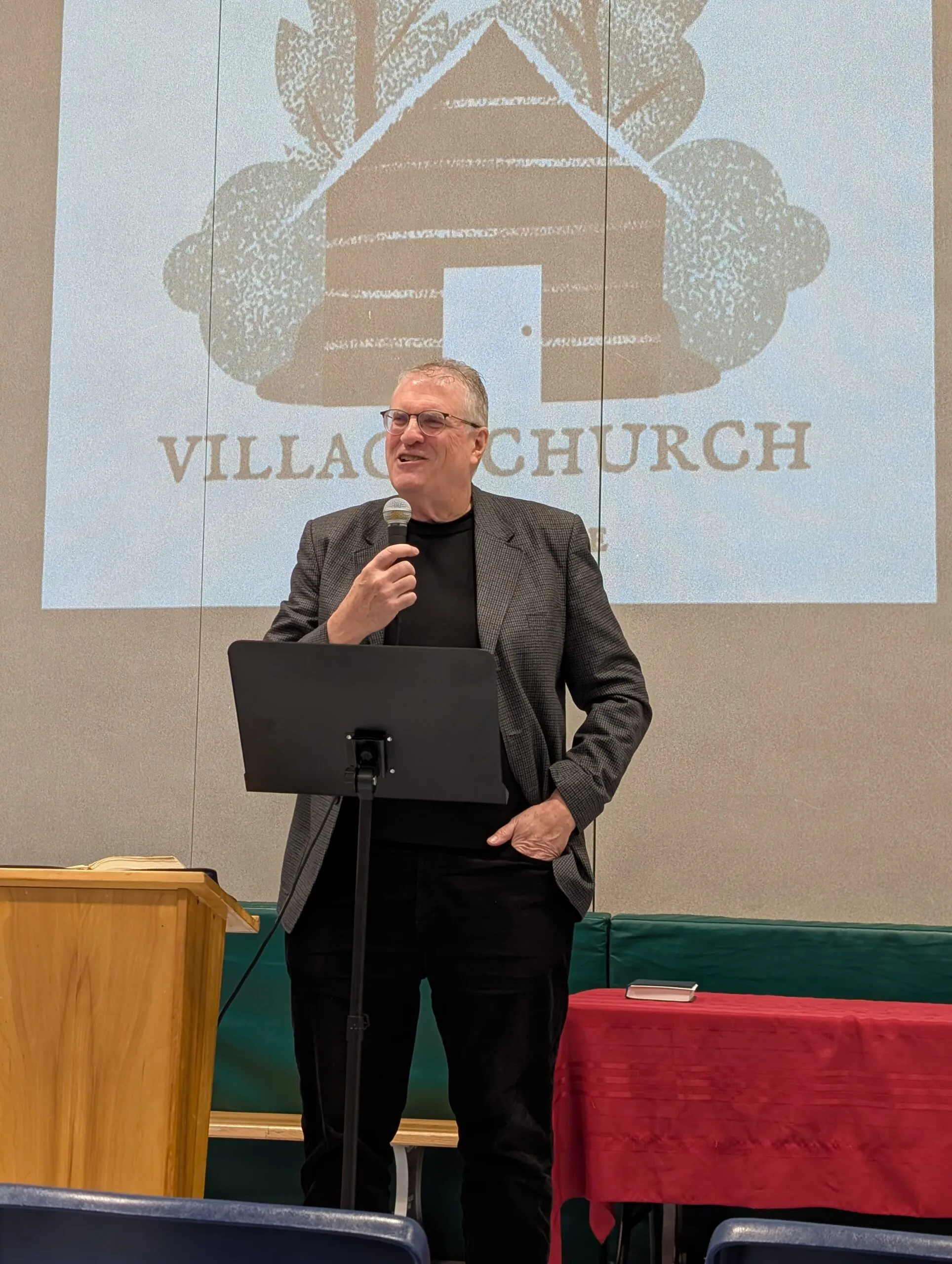 Brian Jose preaching in front of the Village Church logo